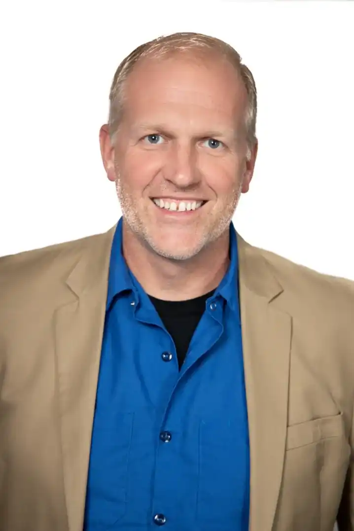 Mike Schneider, founder and president of Schneider Painting, in a tan blazer over a blue shirt against a white background