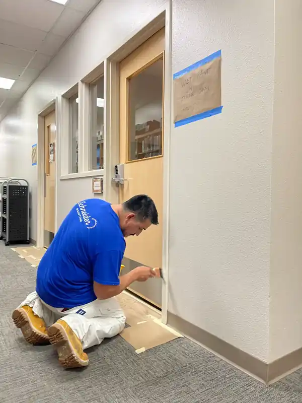 Painter kneeling to paint a commercial door frame with the floor protected