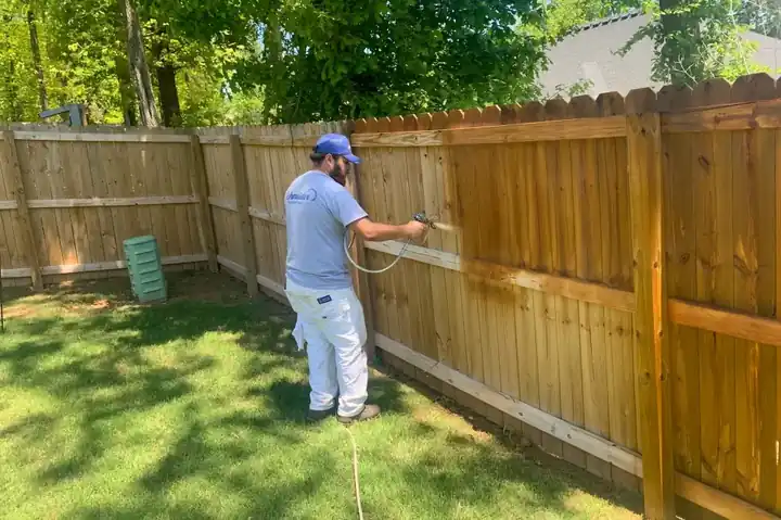 Painter spraying stain on a privacy fence