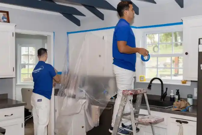 Two Schneider painters masking kitchen cabinets with paper and tape