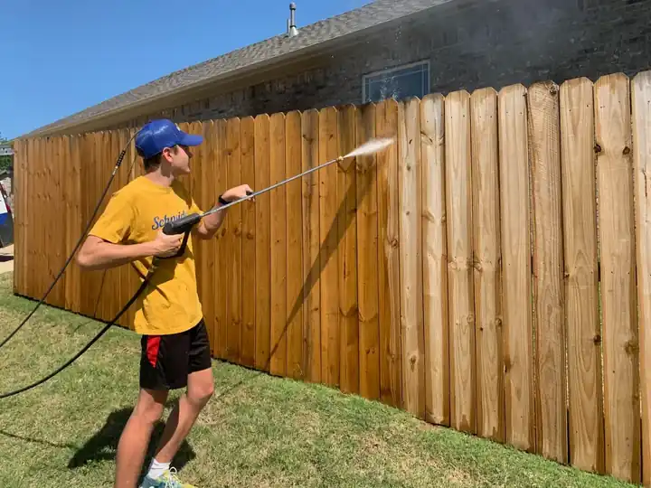 A Schneider crew member pressure-washing a fence before staining