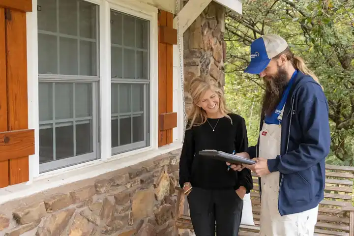 A Schneider painter with a clipboard consulting a homeowner on a stone porch