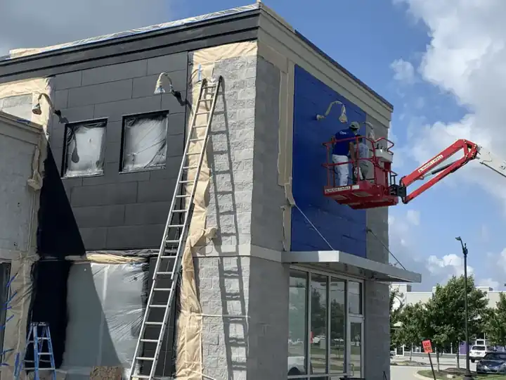 Commercial repaint in progress on a blue facade, with ladders and a crew on a boom lift